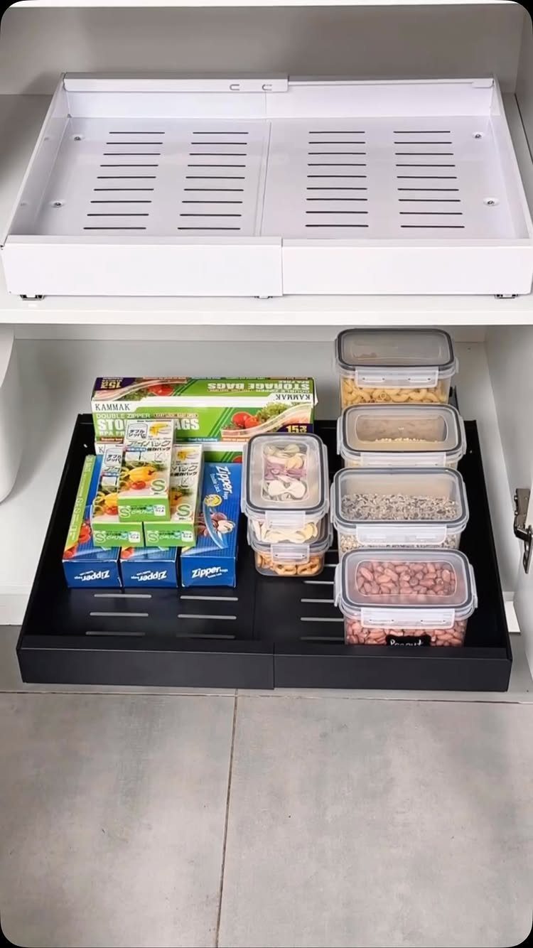 Deep black roll-out cabinet tray filled with food boxes and plastic storage containers.
