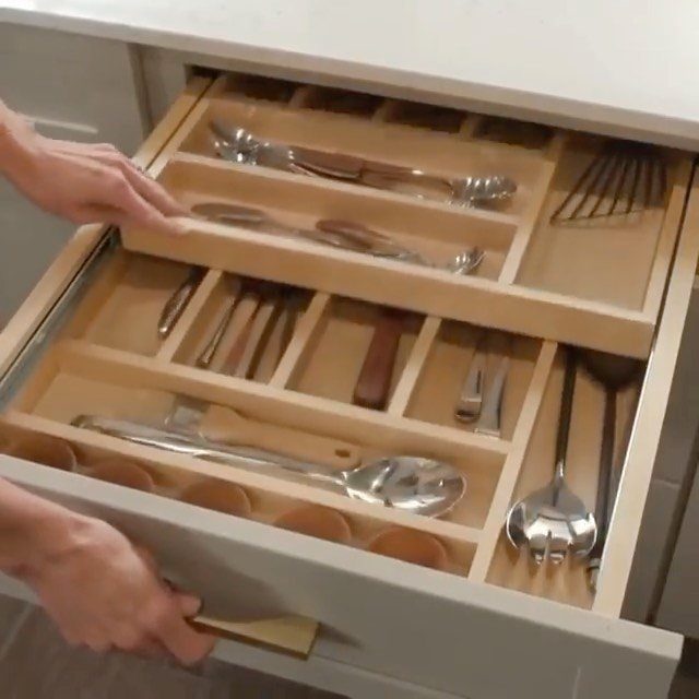 Open kitchen drawer with wooden dividers organizing various metal serving utensils and ladles.
