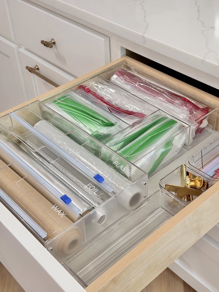 Open kitchen drawer with clear organizers holding foil, wax paper, and plastic bags.