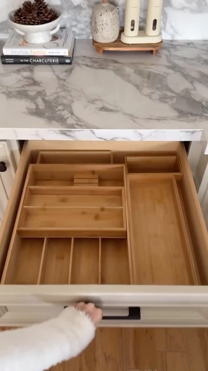 Open white kitchen drawer featuring light wood organizers and dividers for utensil storage.