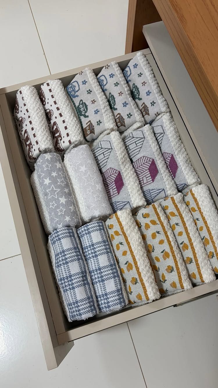 Neatly folded and rolled kitchen towels organized in a white storage drawer.