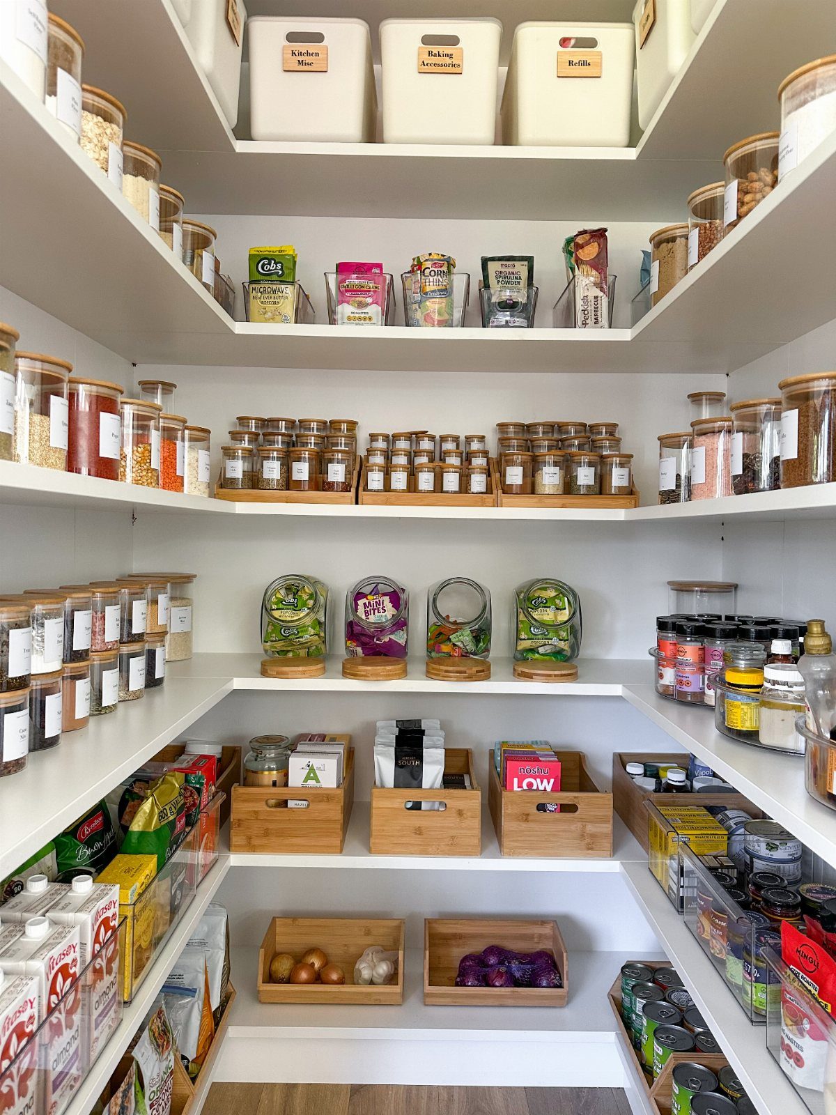 Organized white walk-in pantry with glass jars, wooden crates, and labeled storage bins.