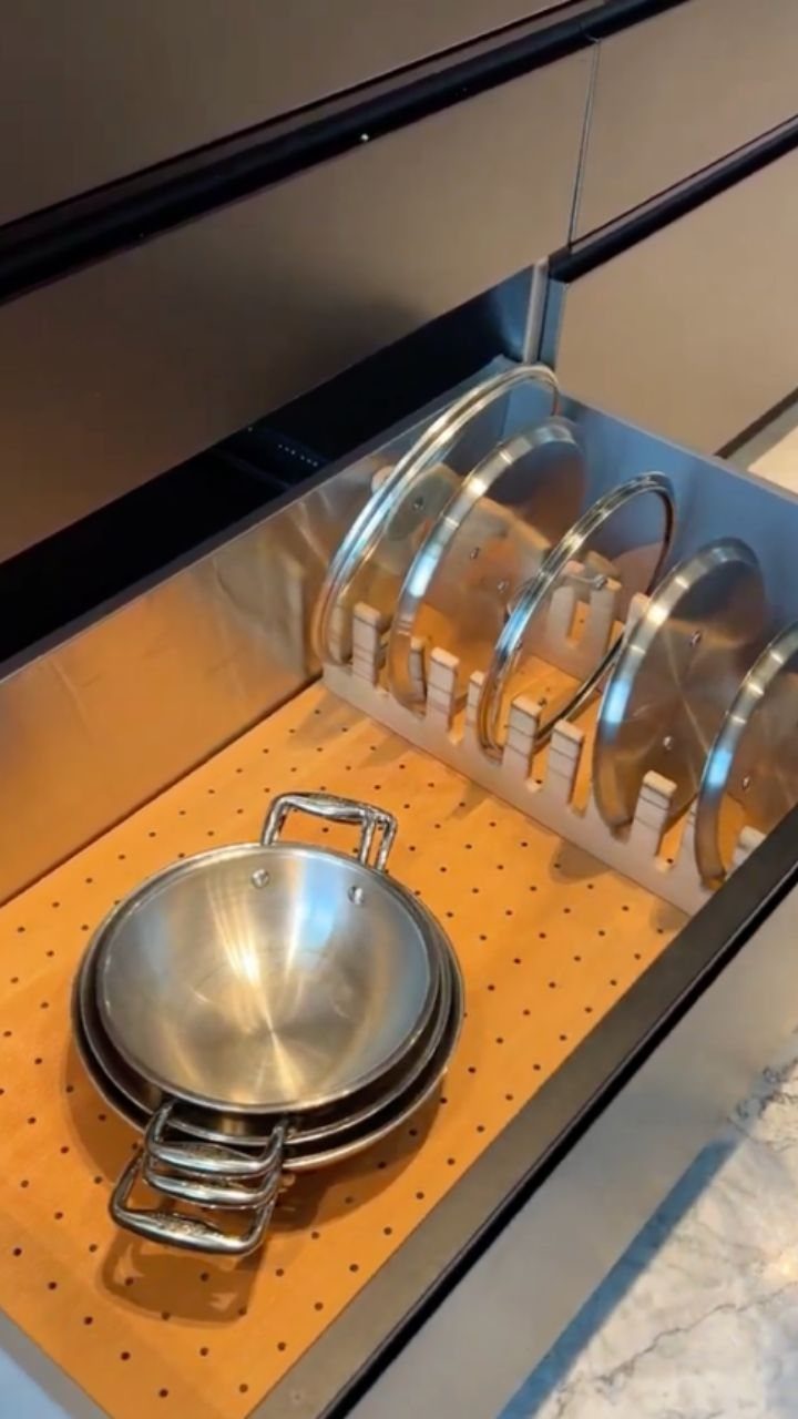 Pots and lids organized in a kitchen drawer with a pegboard base.