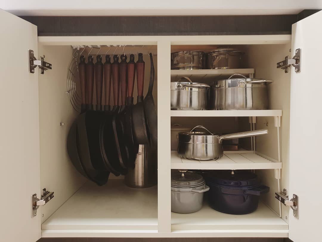 Kitchen cabinet with pots and pans hanging on a rack and stored on shelves.