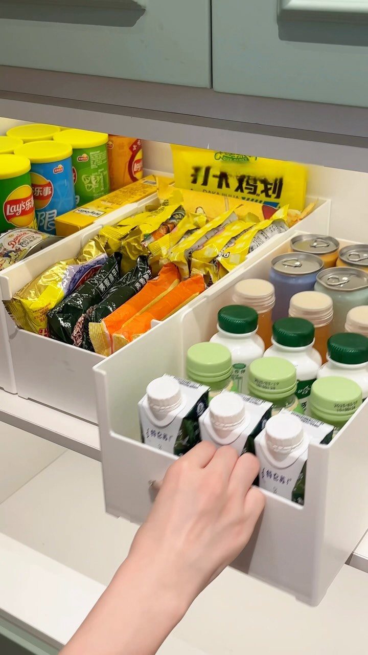 White plastic organizer bins in a kitchen drawer holding snacks and small bottles.