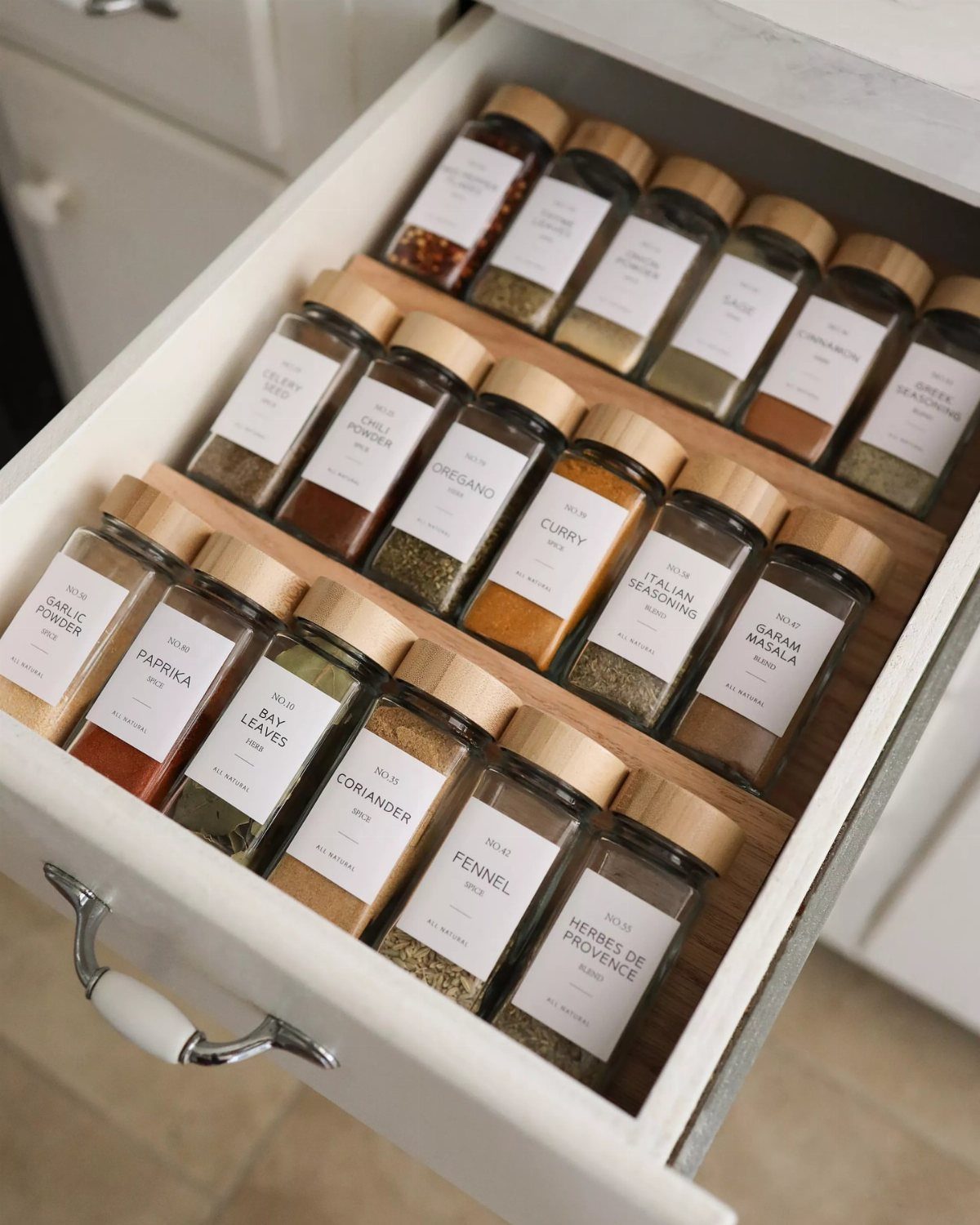 Open white kitchen drawer with neatly organized glass spice jars in wooden dividers.