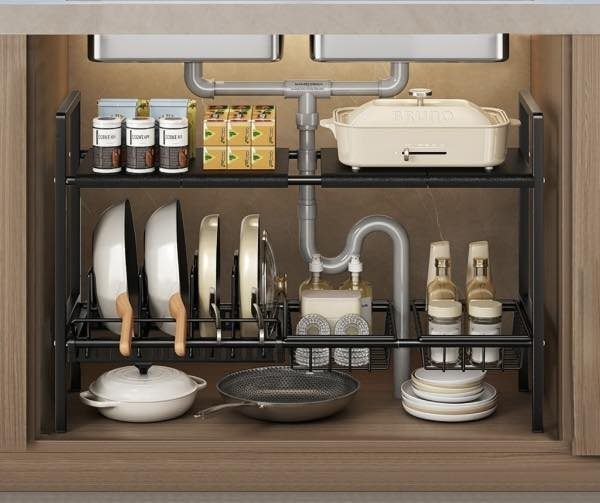 Black metal under-sink organizer holding pots and pans around grey plumbing pipes.