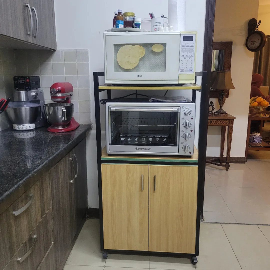 Rolling kitchen cart holding a white microwave and a toaster oven in a kitchen.