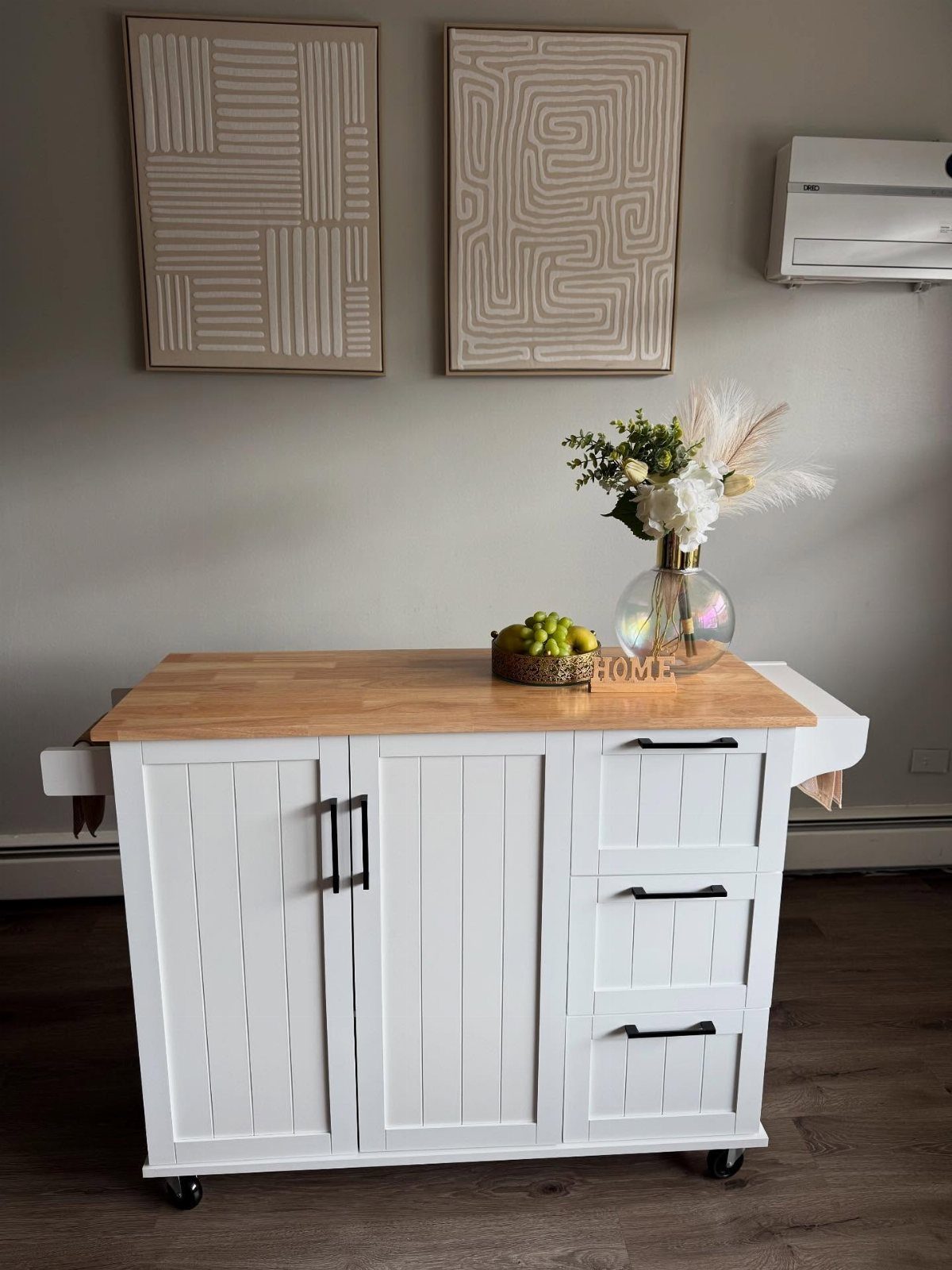White wooden kitchen island cart with wood top and black handles on wheels.