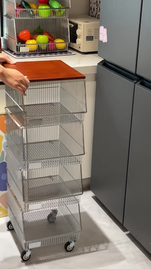 Four-tier silver wire-basket storage cart with wooden top next to a grey refrigerator.