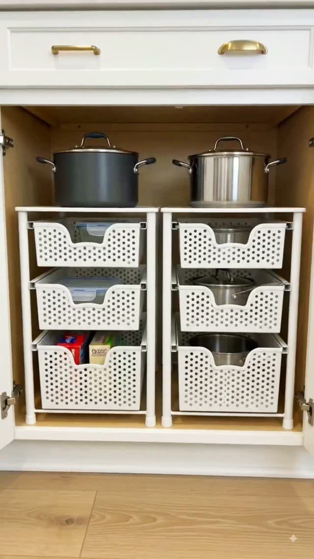Two white three-tier storage drawers inside a white kitchen cabinet with pots on top.