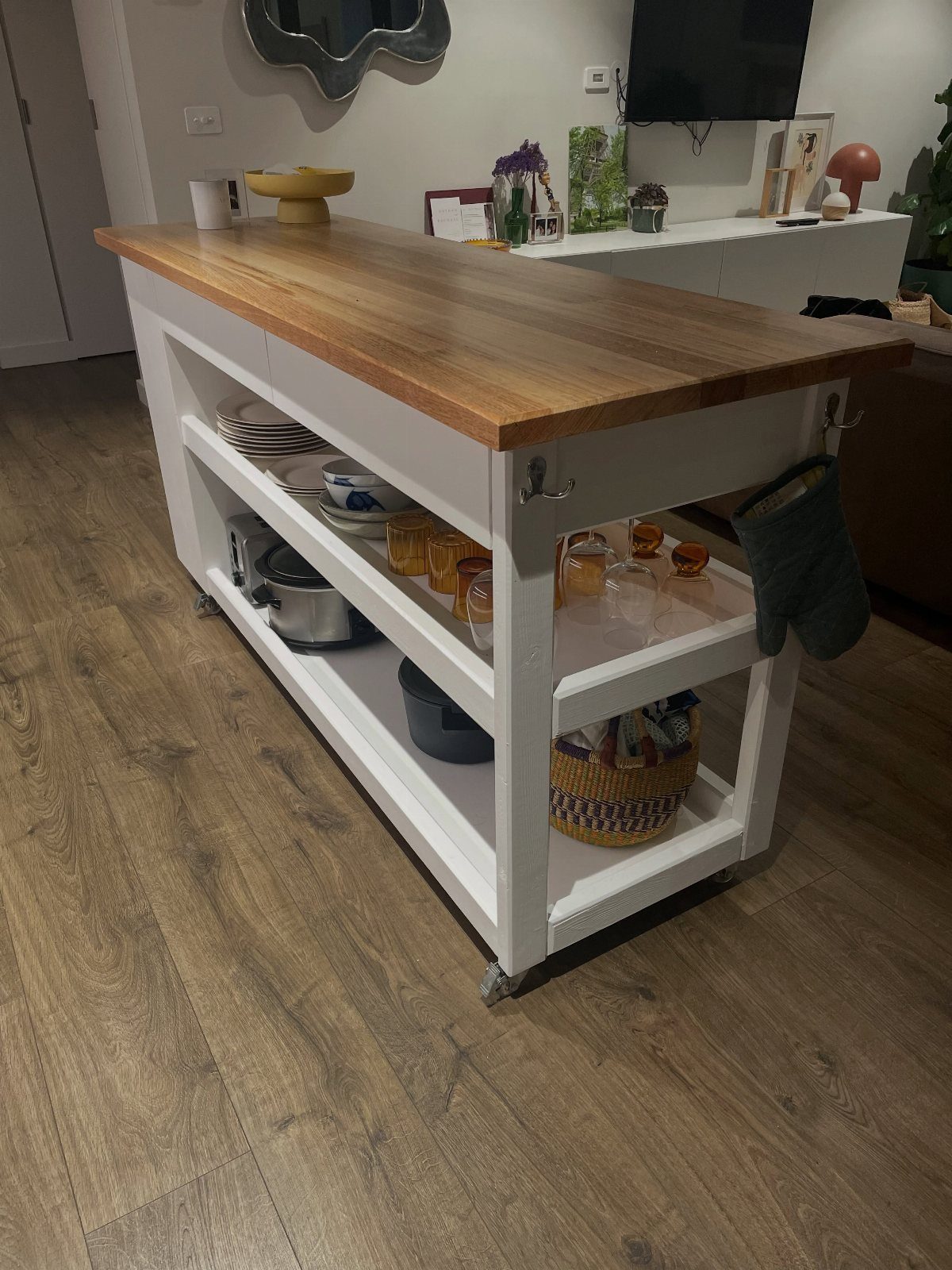 White wooden kitchen island with wood top and open shelves on a wooden floor.