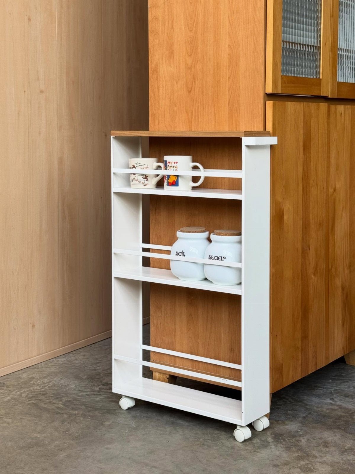 White Yamazaki storage cart with wooden top holding mugs and canisters in a kitchen.