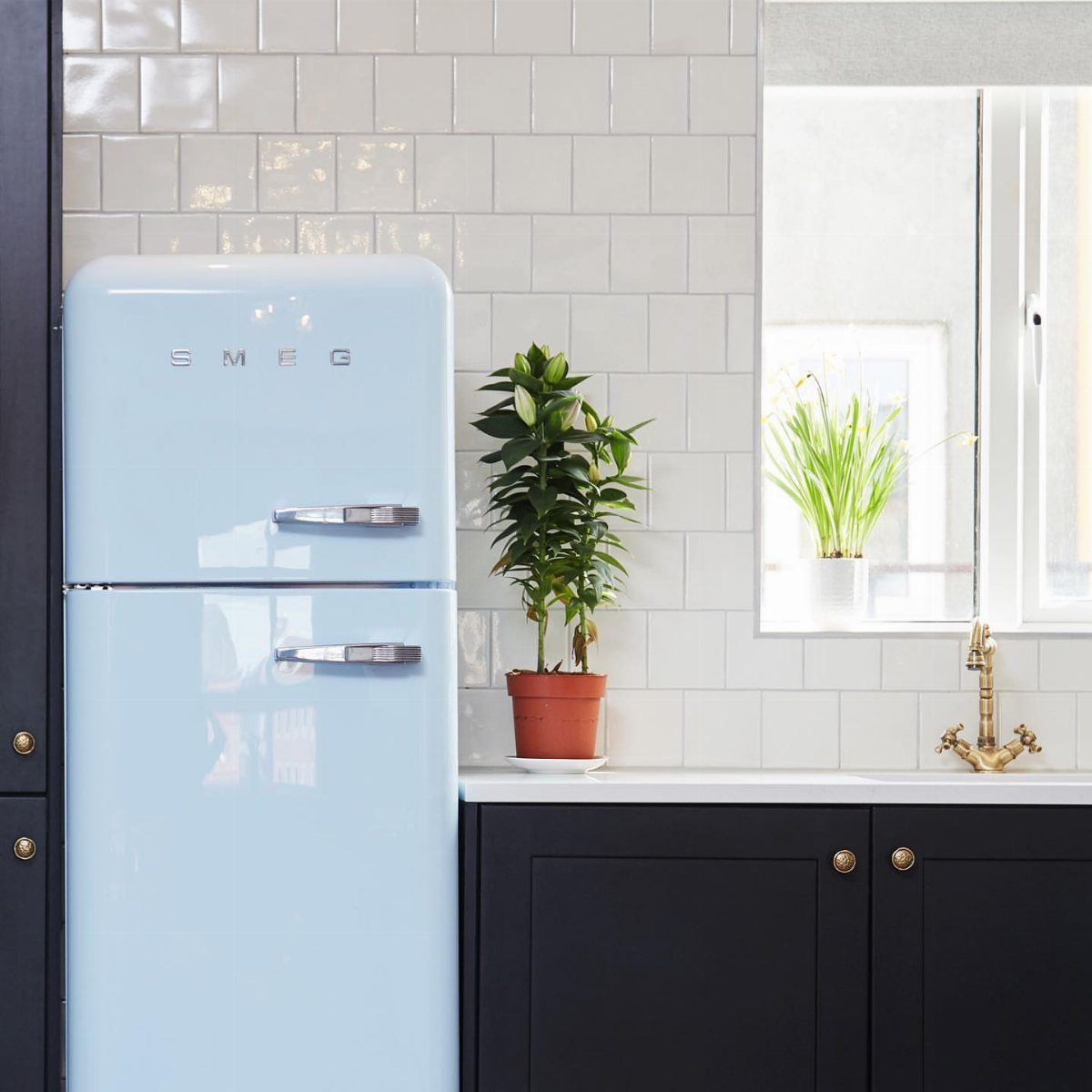Light blue retro Smeg refrigerator next to navy blue cabinets and white tiled wall.