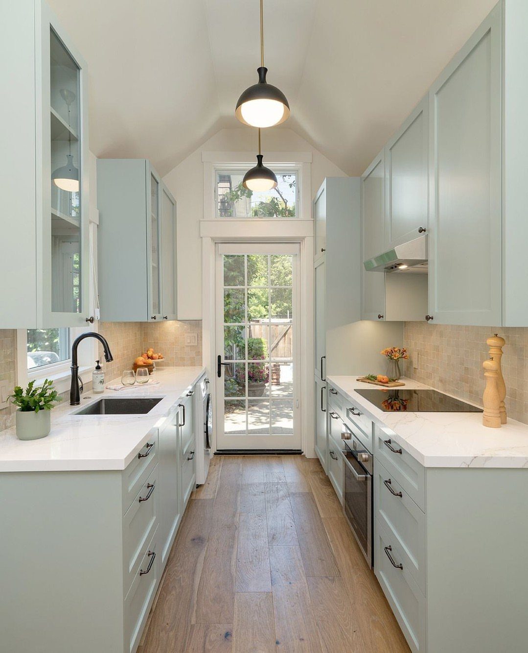 Narrow galley kitchen with light blue cabinets, white countertops, and wooden floors.