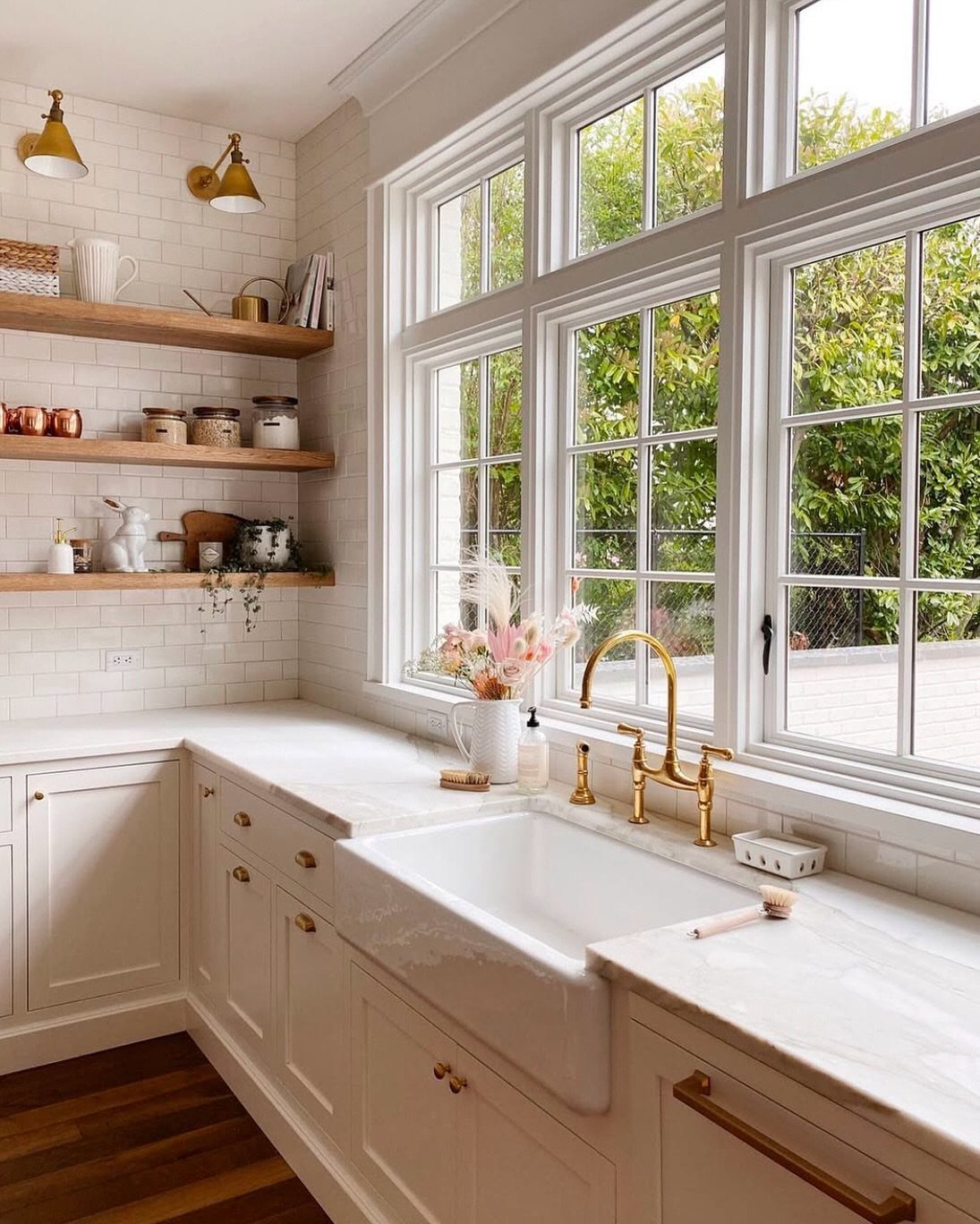 White apron-front farmhouse sink with gold faucet in a bright cottage kitchen.
