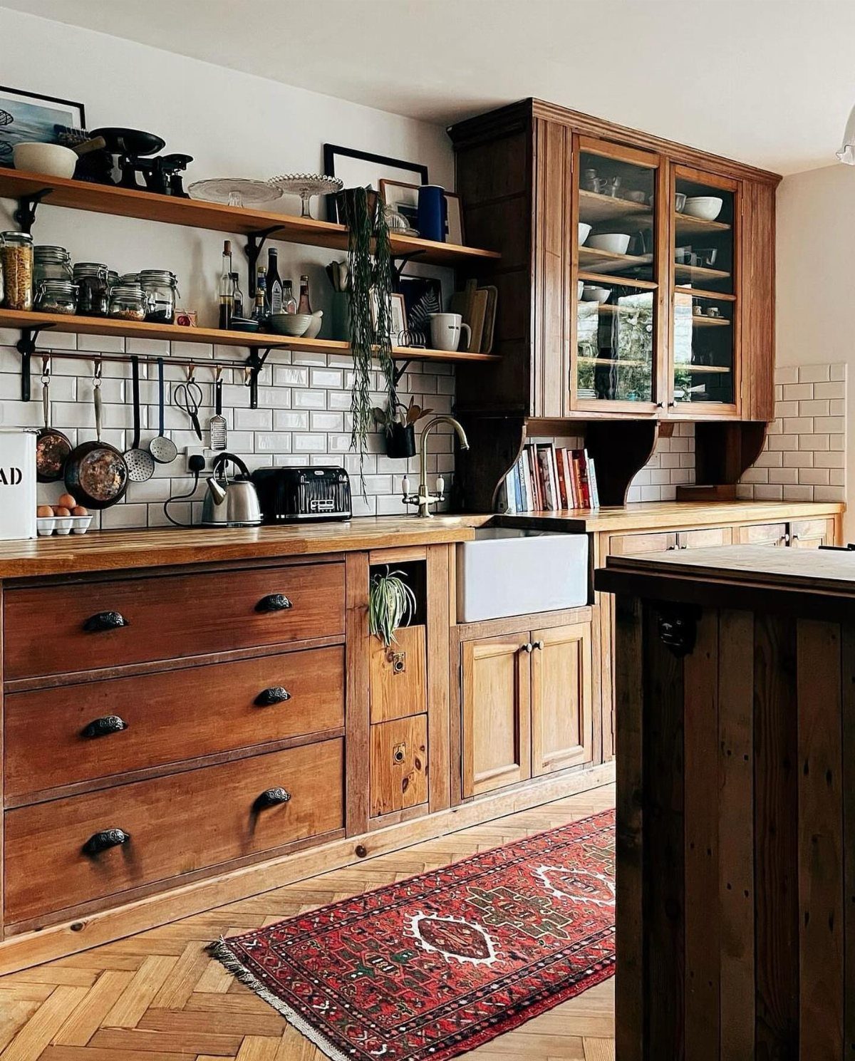 Wooden open shelves with glassware above a rustic kitchen counter and farmhouse sink.
