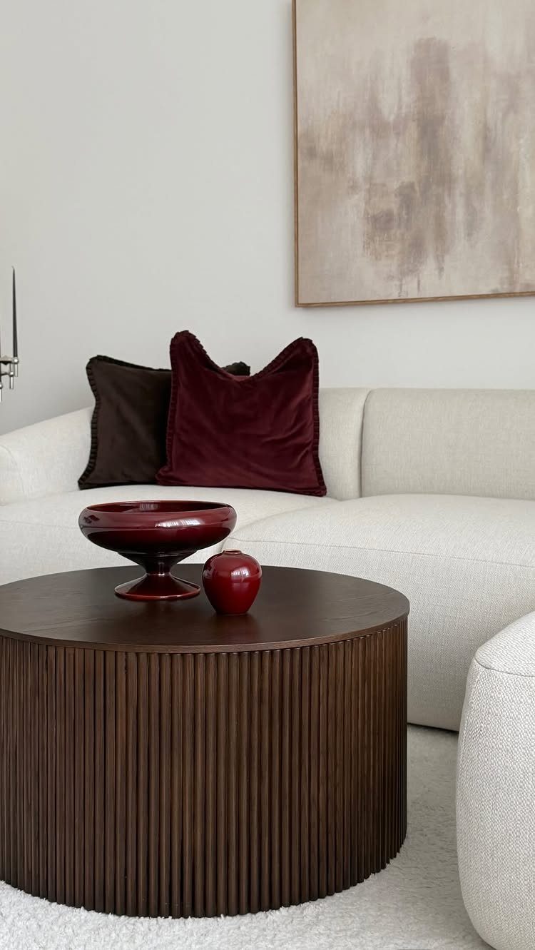 White sofa with burgundy velvet pillows and a dark wood fluted coffee table.