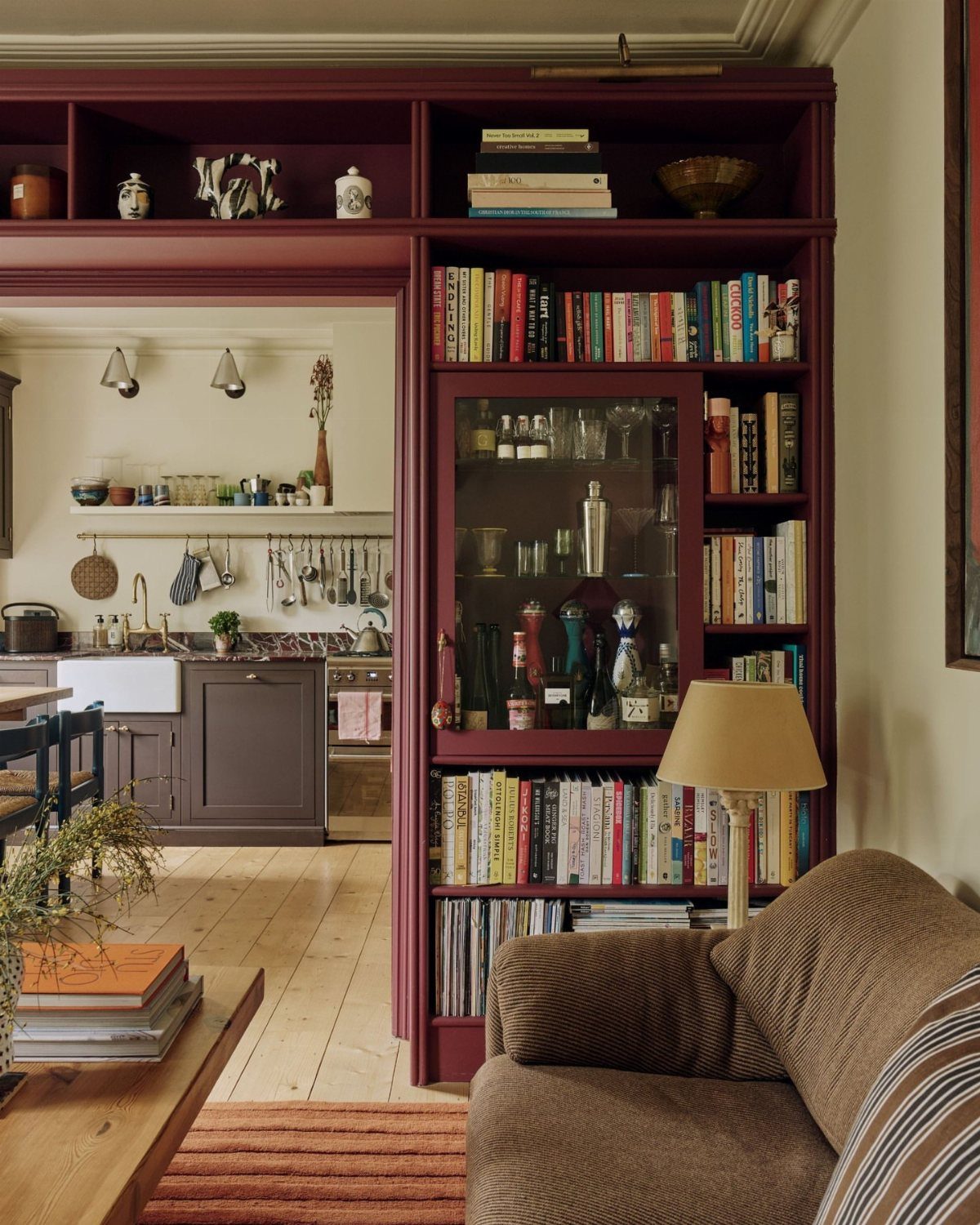 Burgundy built-in shelving filled with books and glassware next to a kitchen area.