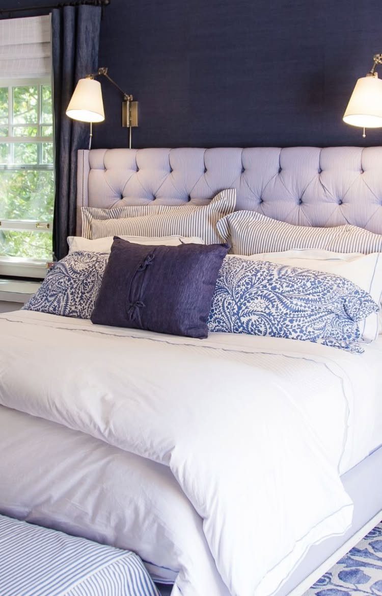 Navy blue walls and curtains in a bedroom with white bedding and grey headboard