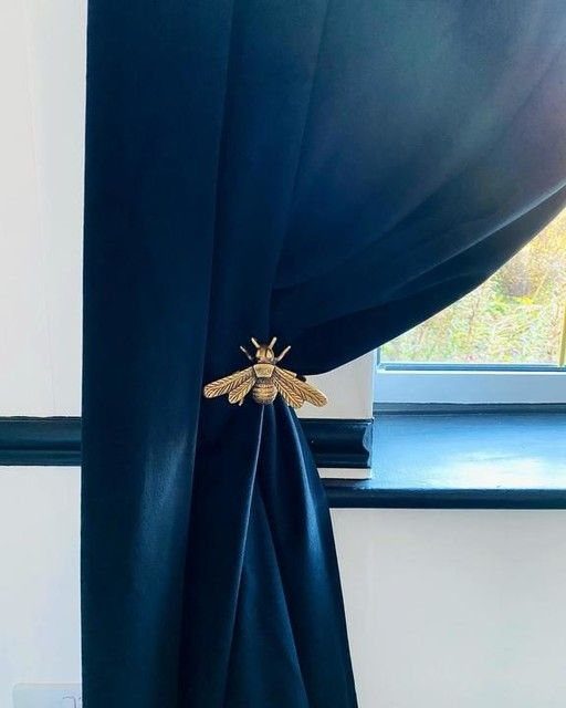 Navy blue velvet curtains held back by a gold bee-shaped curtain tie-back.