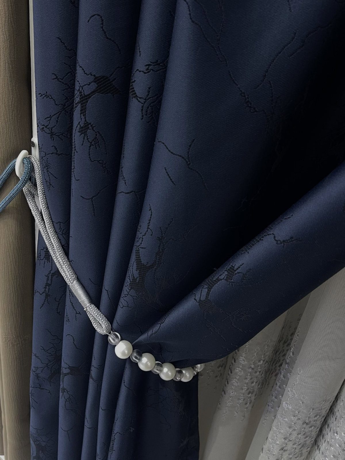 Navy blue patterned curtains held back by a silver pearl tieback.