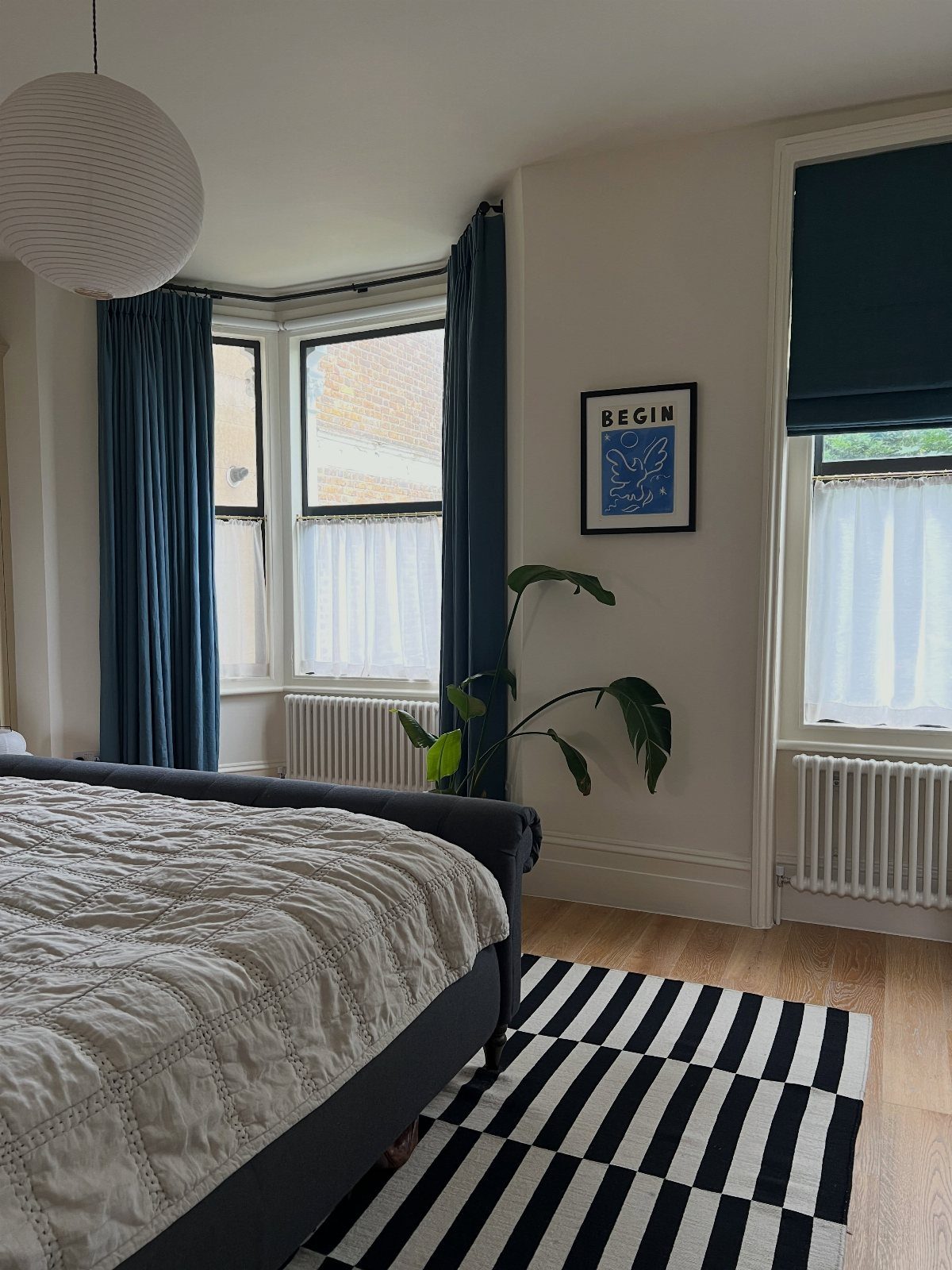 Navy blue curtains and roman shades in a modern bedroom with striped rug.