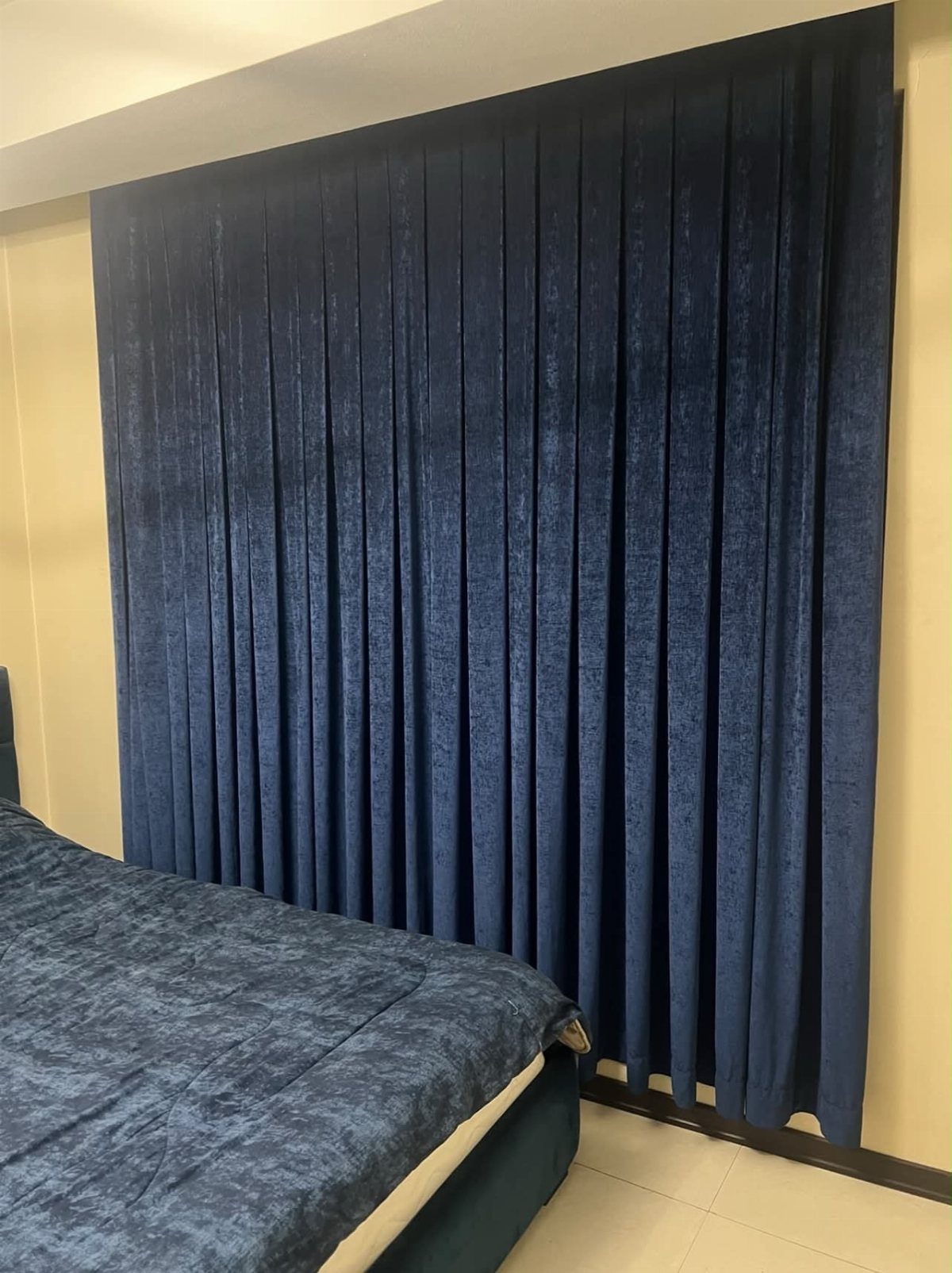 Navy blue velvet curtains covering a bedroom wall next to a navy bed.