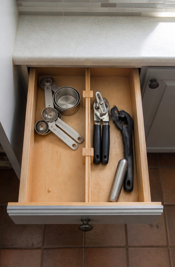 Kitchen drawer with adjustable dividers separating measuring cups and utensils
