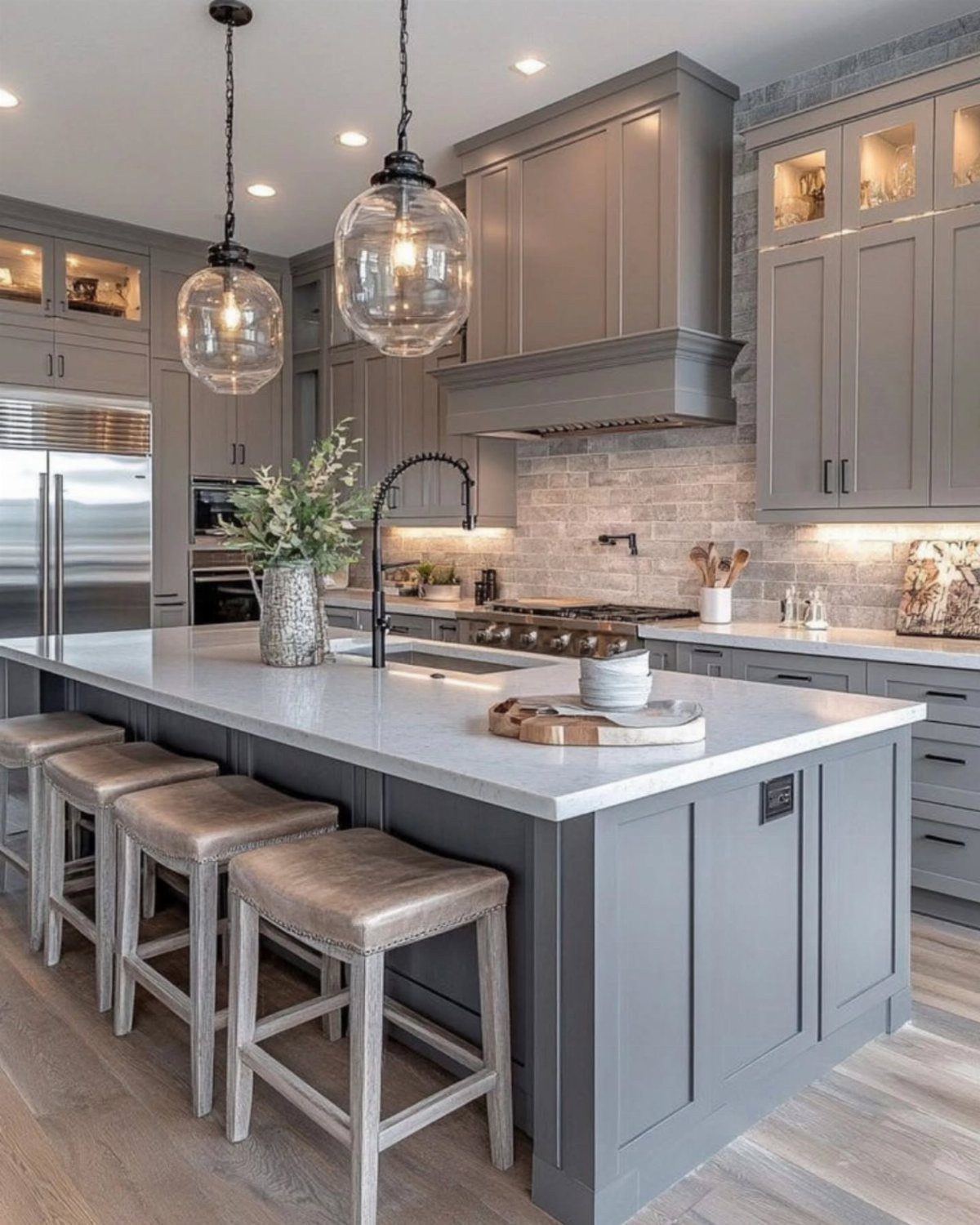 Grey kitchen cabinets and island with white countertops and glass pendant lighting.