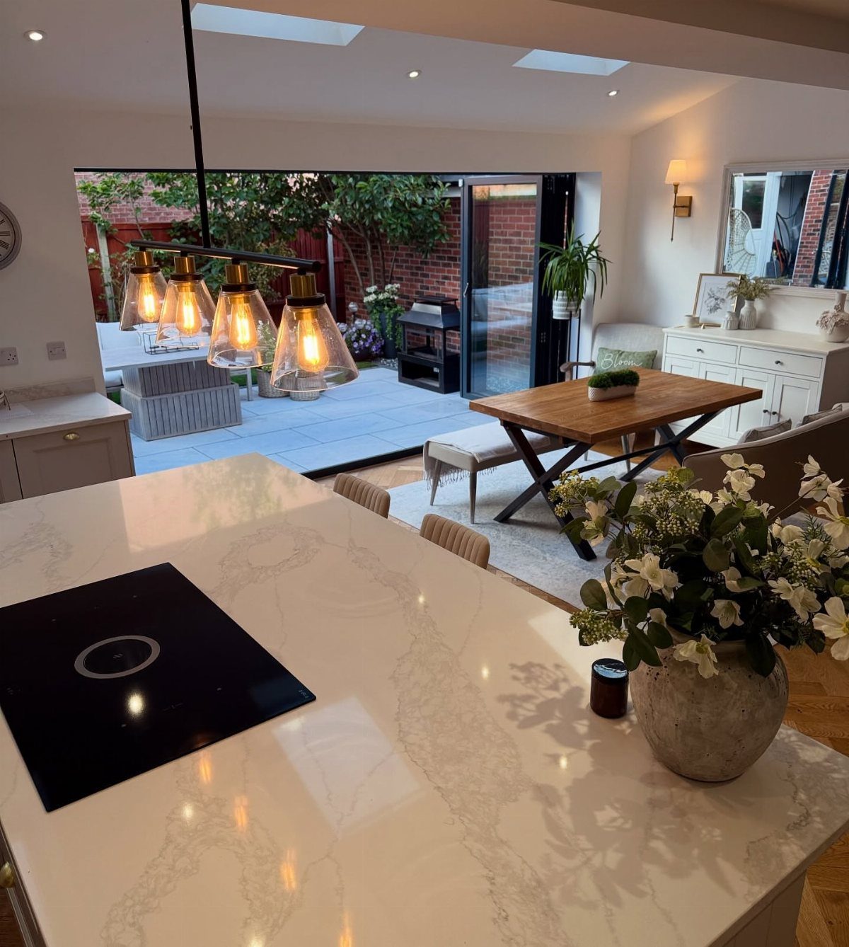 White marble kitchen island with induction hob and flowers in an open plan room.
