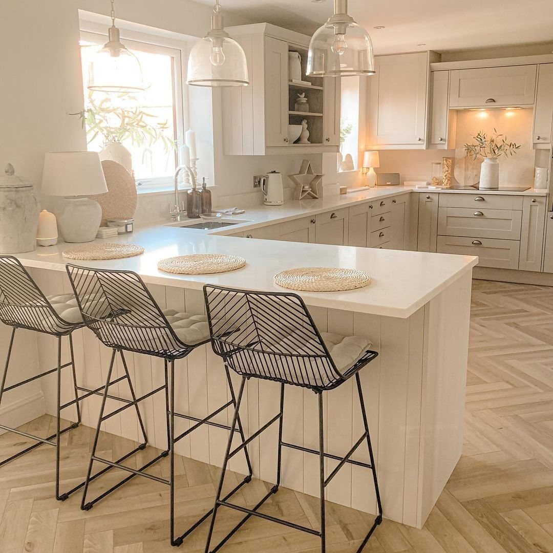 White kitchen peninsula with black wire bar stools and herringbone wood flooring.