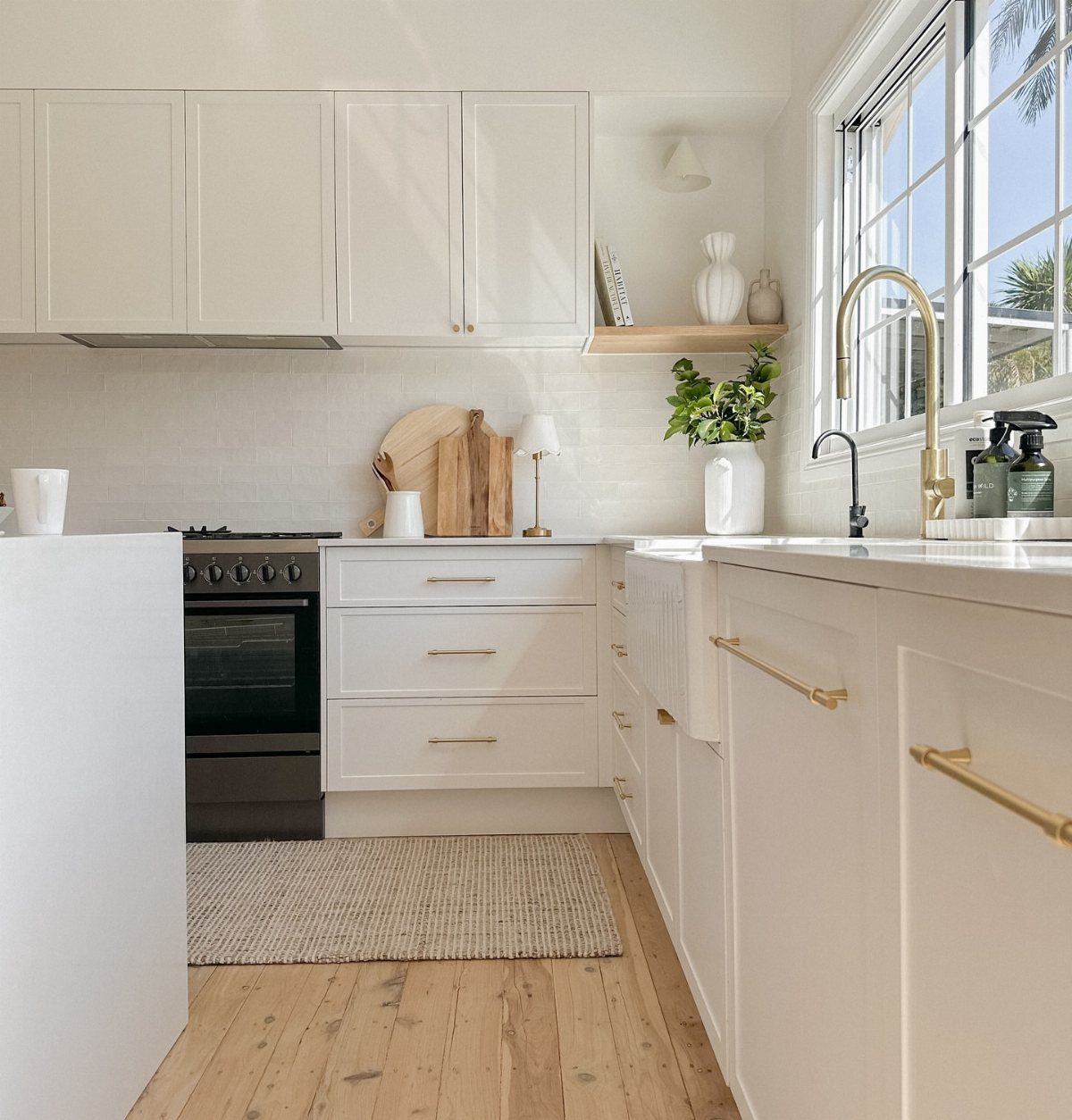White kitchen cabinets and light wood floors with gold hardware and white tiles.