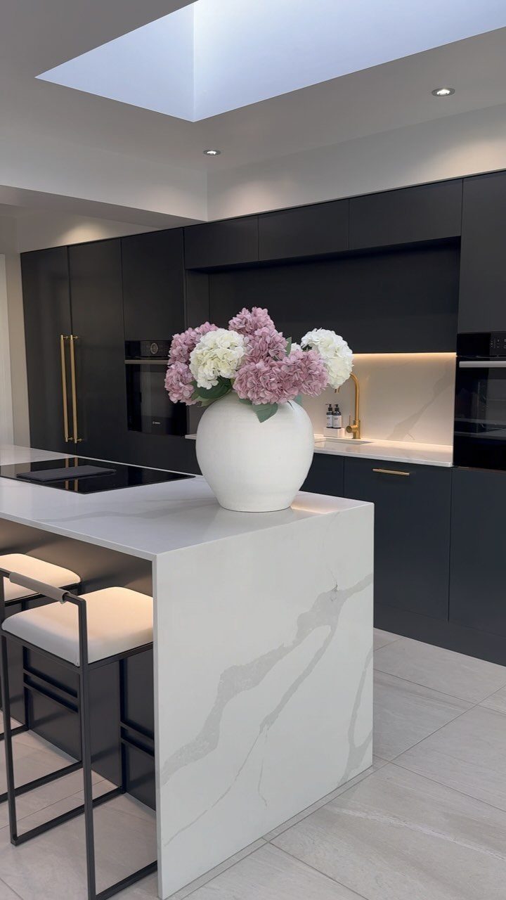 Modern kitchen with matte black cabinets and a white marble-veined island with flowers.