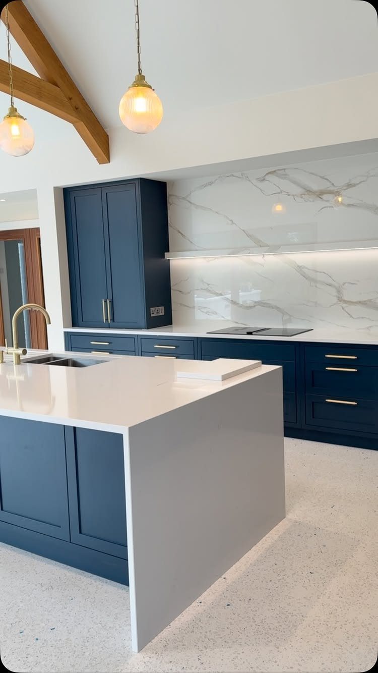 Navy blue kitchen cabinets with white countertops and warm wood ceiling beams.
