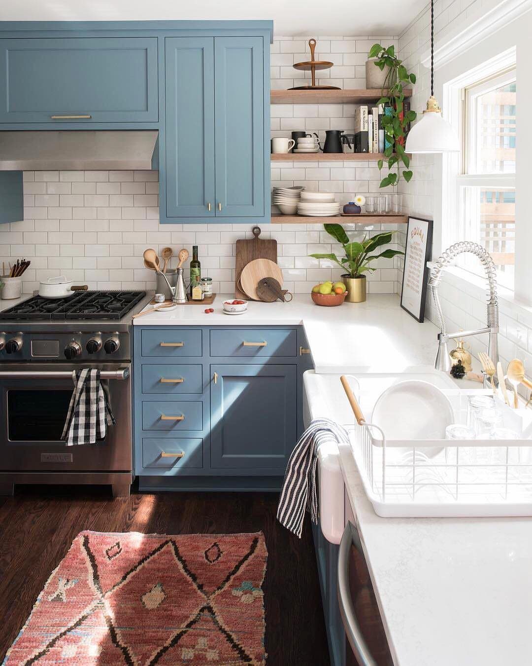 Bright blue kitchen cabinets with white countertops, white tile backsplash, and wooden shelving.