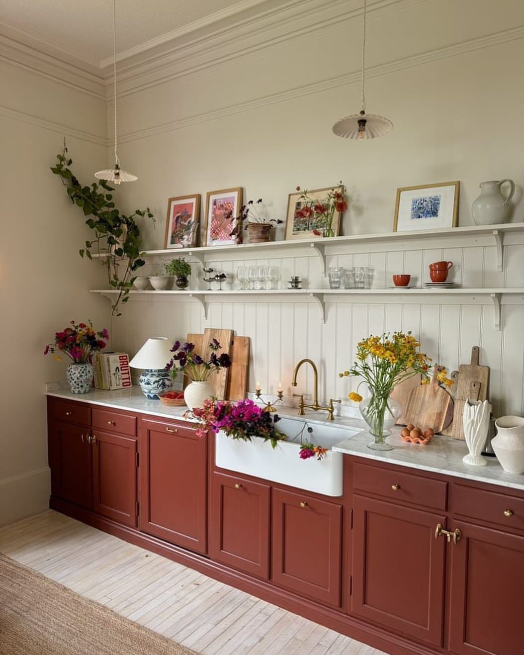 Deep red kitchen cabinets with white marble countertops and colorful floral arrangements.