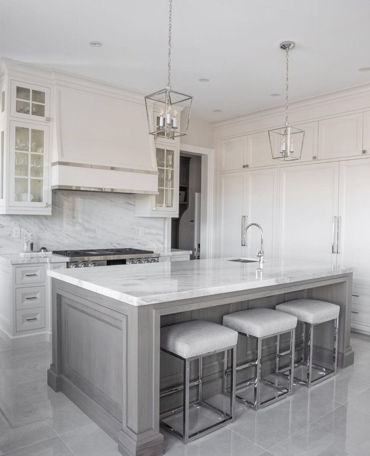 Gray kitchen island with white marble top and white cabinets in a bright room
