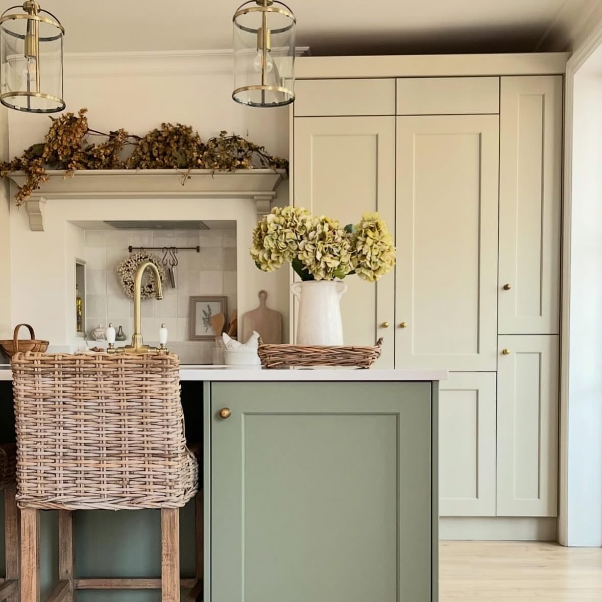 Sage green kitchen island and cream cabinets with a woven wicker bar stool.