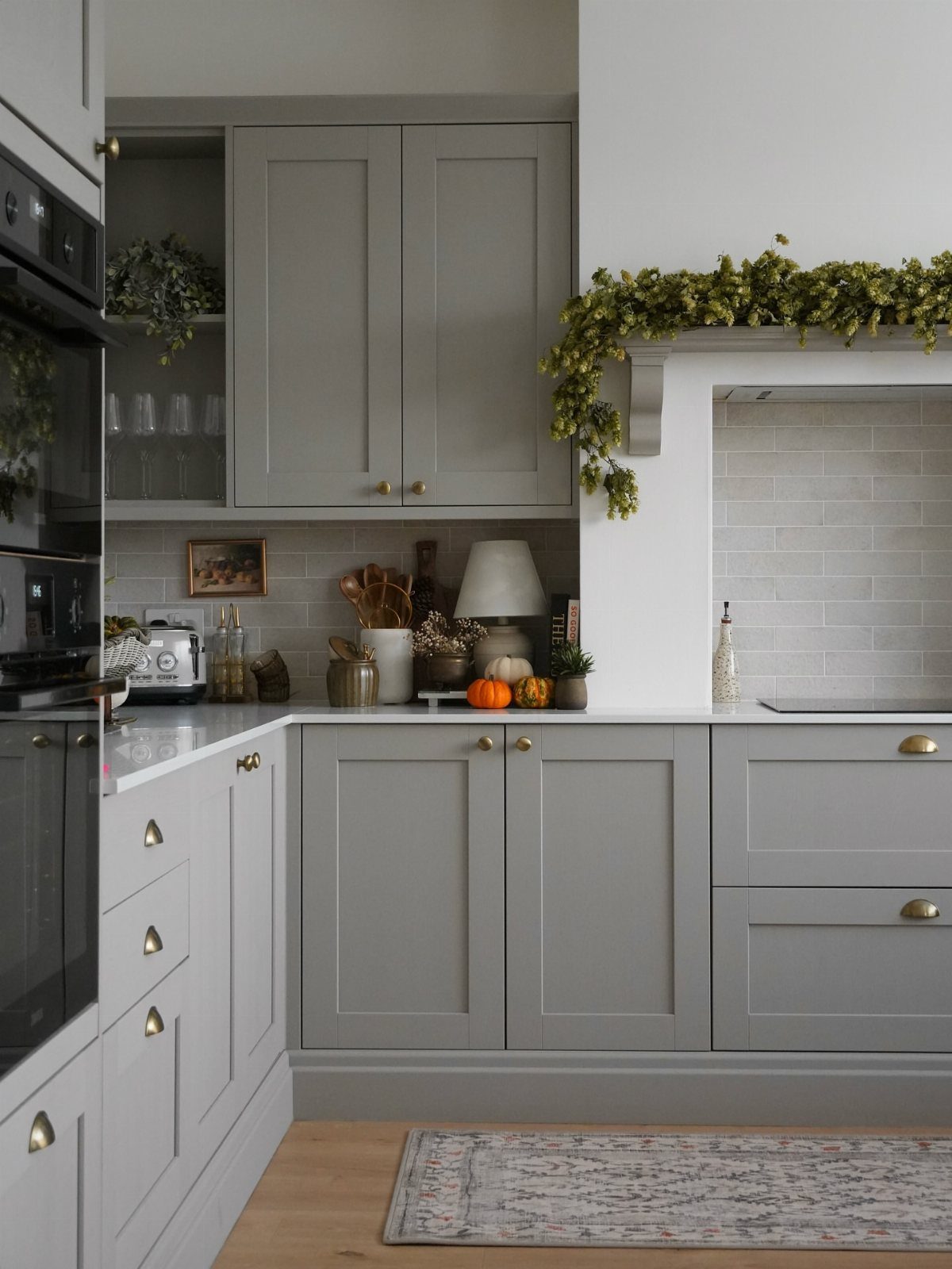 Warm gray shaker cabinets with gold hardware and white countertops in a bright kitchen.