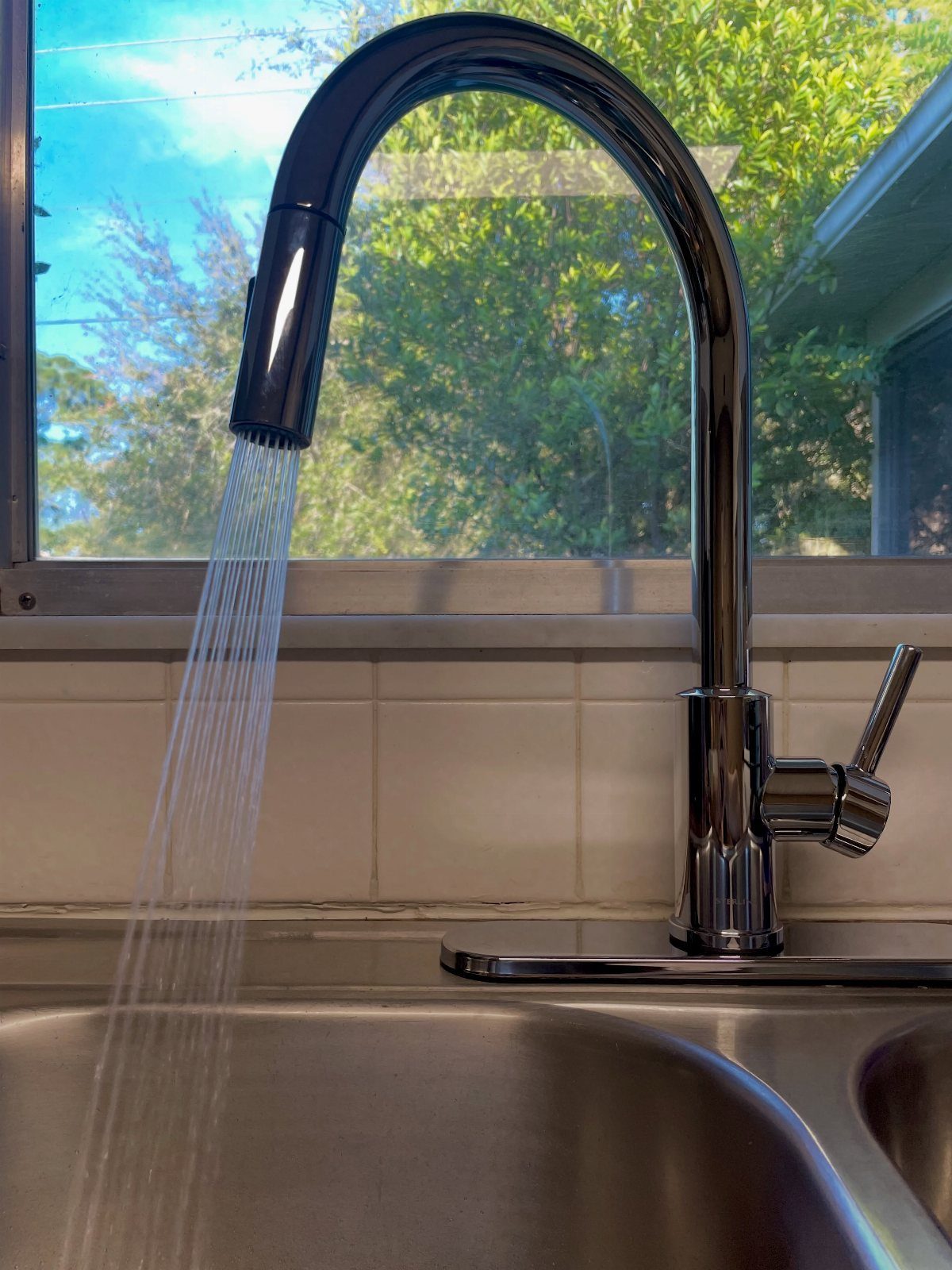 Chrome high-arc pull-down kitchen faucet with water running into a stainless steel sink.