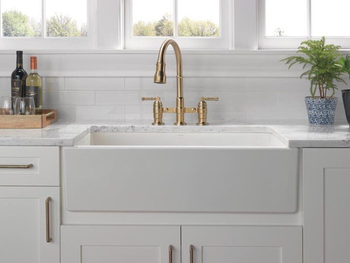 Gold two-handle pull-down kitchen faucet installed over a white farmhouse sink.