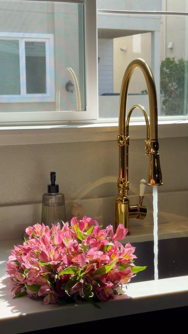 Gold pull-down kitchen faucet running water next to pink flowers on a white counter