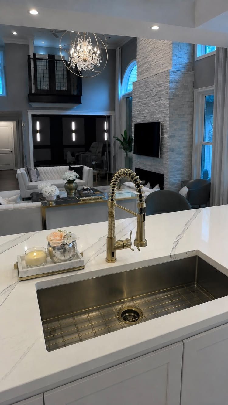 Gold high-arc pull-down kitchen faucet installed on a white marble countertop with sink.