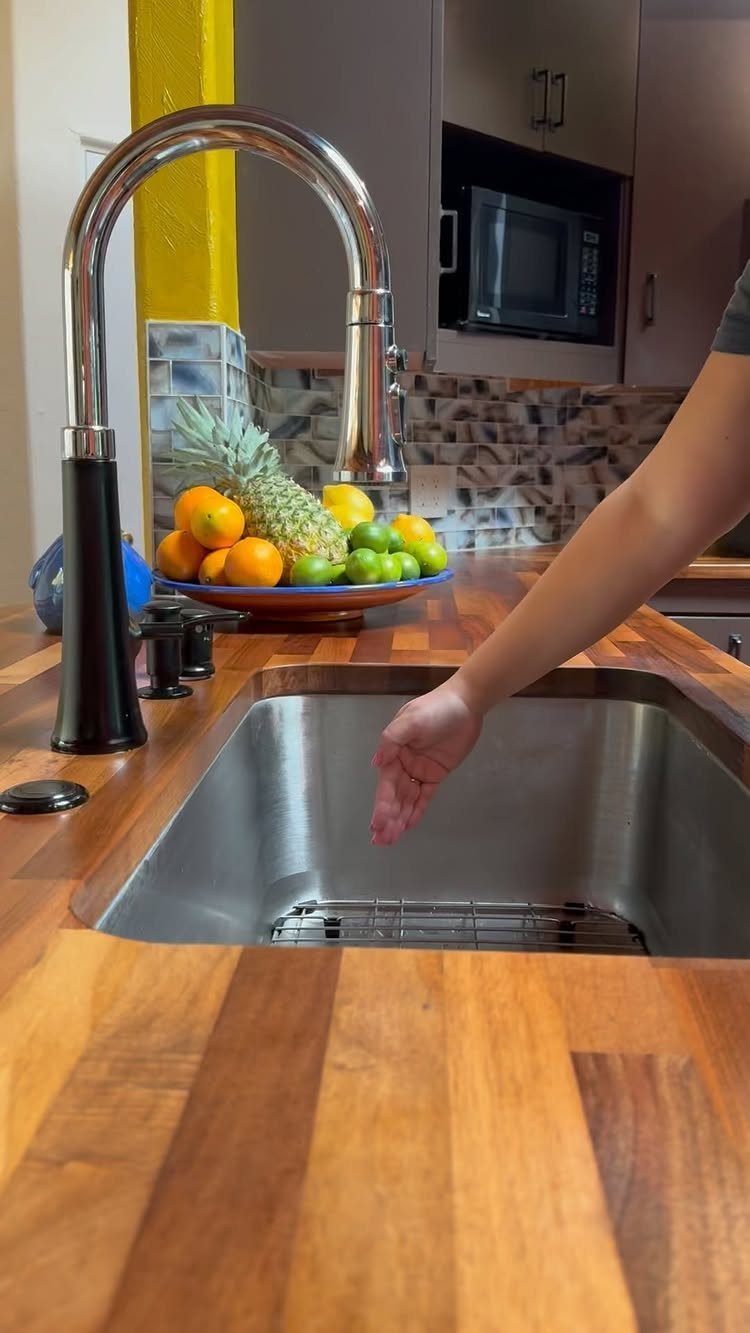 Chrome high-arc kitchen faucet on a wooden countertop next to a stainless steel sink.