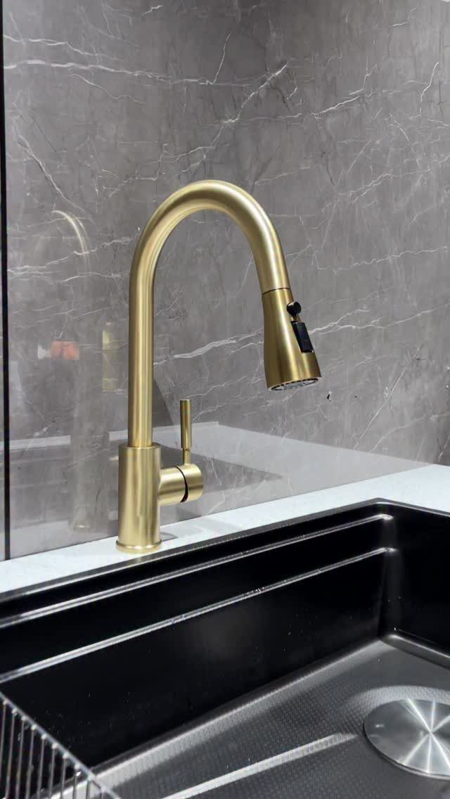 Gold high-arc kitchen faucet with pull-down sprayer installed over a black sink.