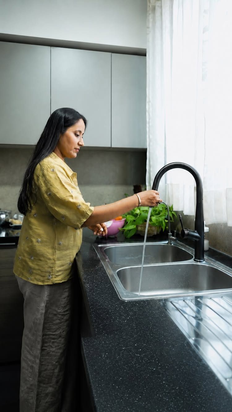Woman rinsing green vegetables in a stainless steel sink with a black faucet.