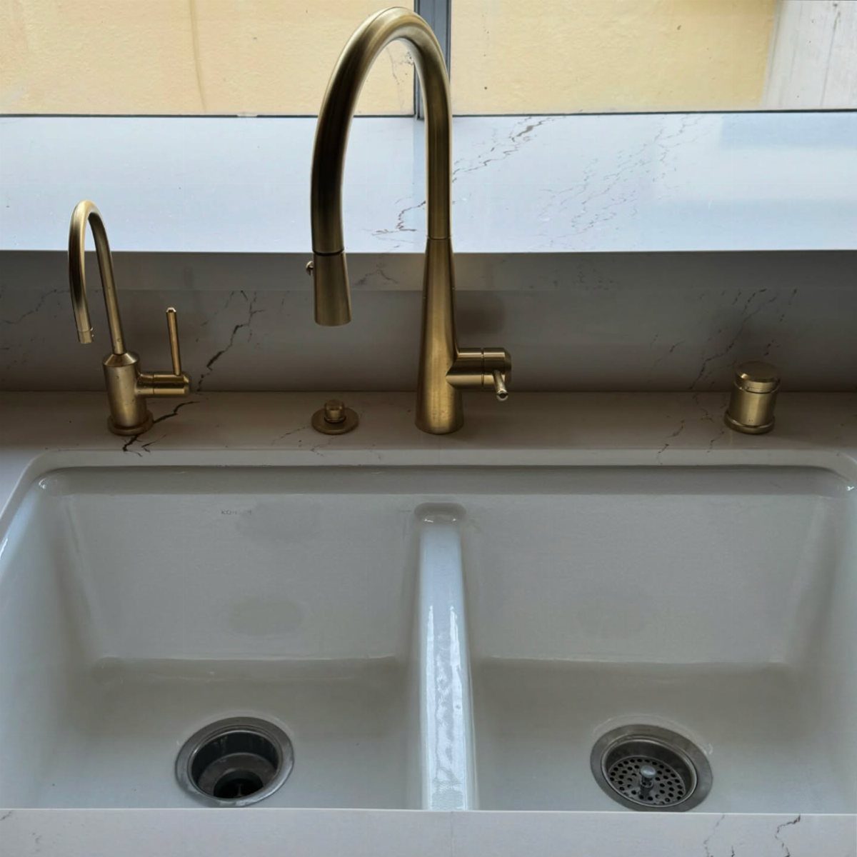 Gold brass high-arc kitchen faucet installed on a white marble countertop with double sink.