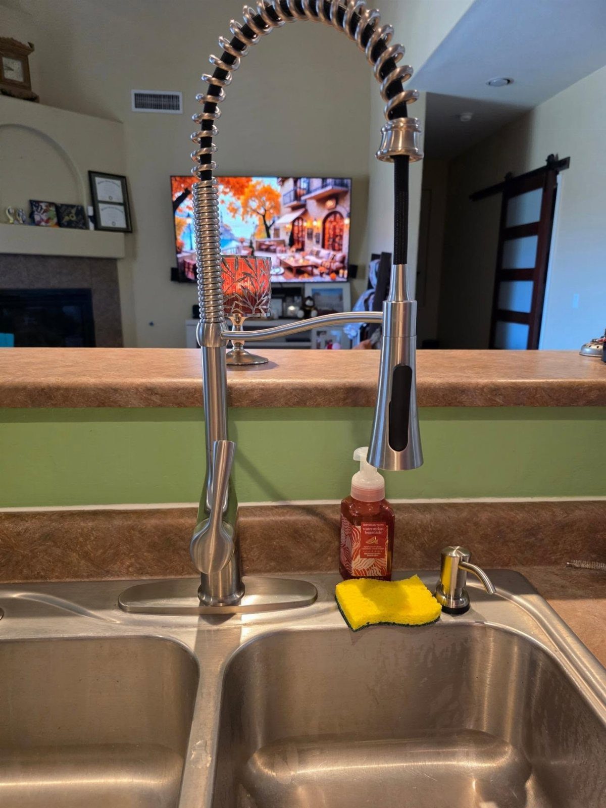 Stainless steel pull-down kitchen faucet with spring neck over a double basin sink.