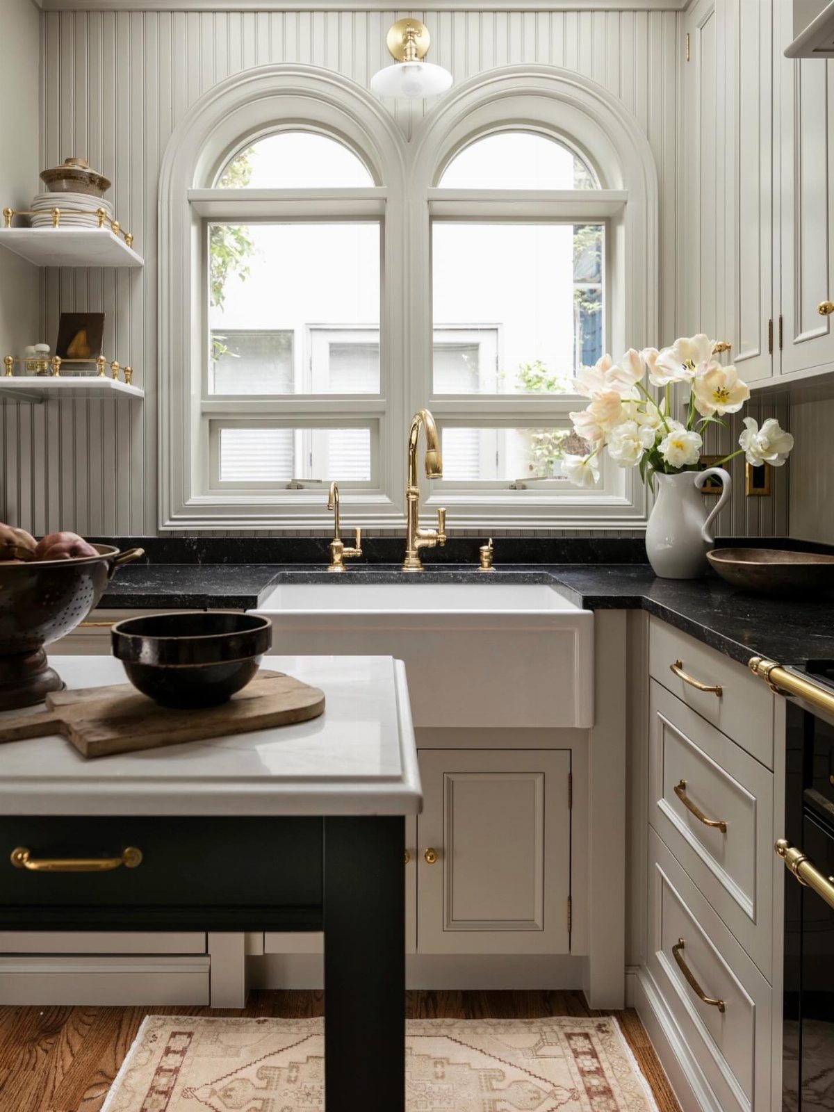 Gold traditional gantry pulldown faucet installed on a black countertop with white farmhouse sink.